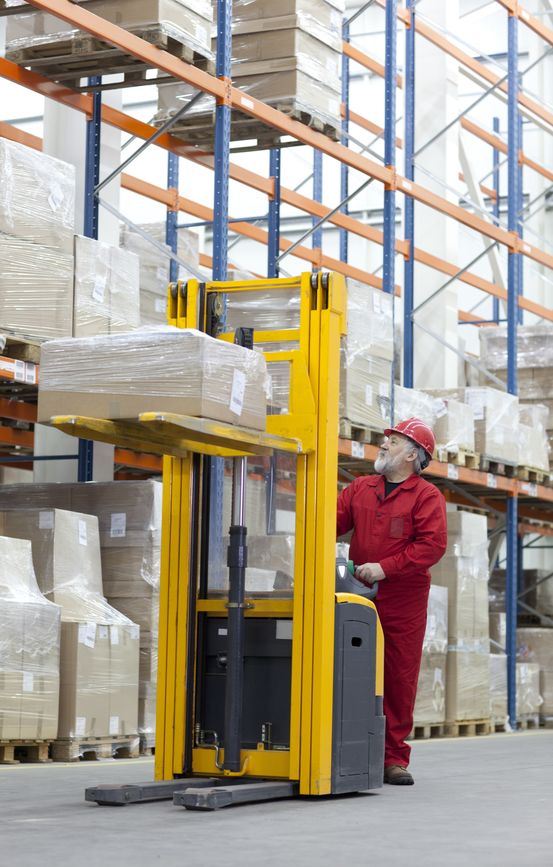 senior worker manual forklift operator in red uniform at work in warehouse