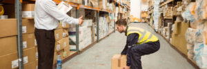 Manager watching worker carrying boxes in a large warehouse