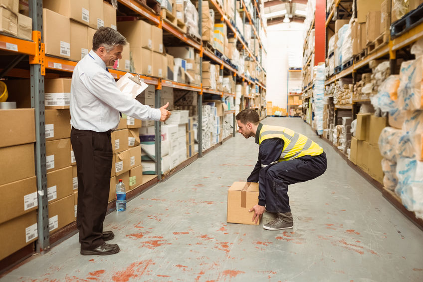 Manager watching worker carrying boxes in a large warehouse