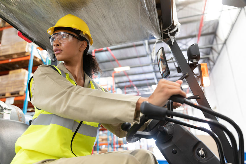 Woman in proper safety attire moving a fork lift in a warehouse 