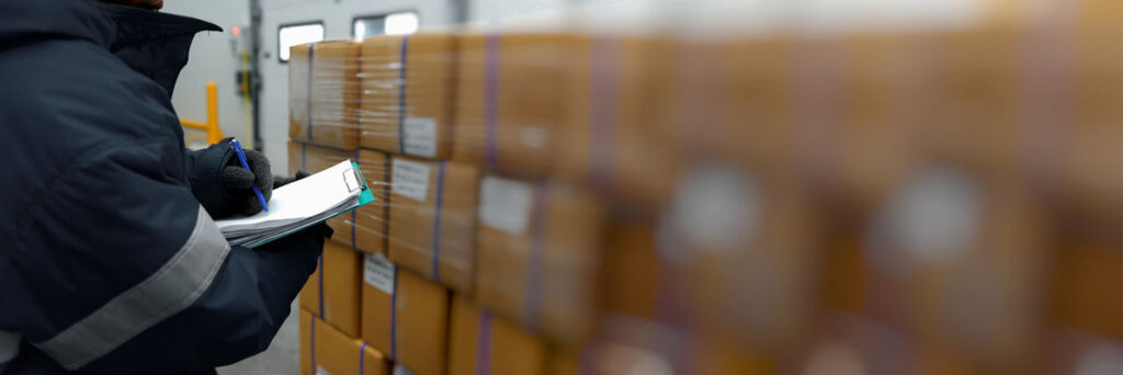 Warehouse worker with a clipboard checking on a stack of boxes