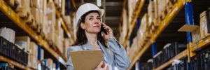 Female warehouse worker talking on her phone while holding a clipboard