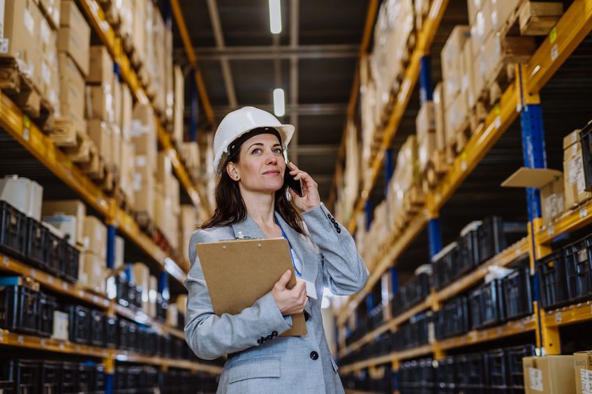 Female warehouse worker talking on her phone while holding a clipboard